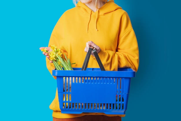 Stylish female in yellow hoodie with blue basket and flowers on blue background