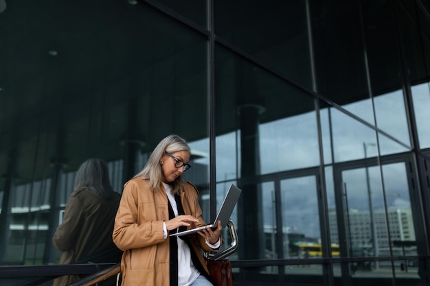 Stylish fifty year old woman working on a laptop at the entrance to the office building