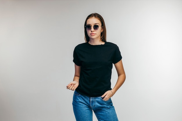 Stylish girl in glasses wearing black t-shirt posing in studio