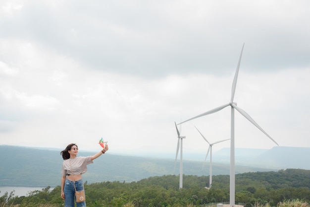 Stylish girl She likes to travel to the windmills at the renewable power station The backdrop is a beautiful mountain windmill