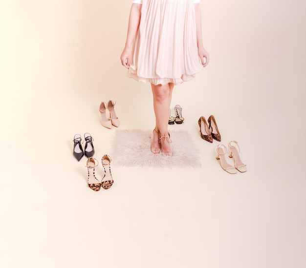 Stylish girl standing in pink pleated dress surrounded by a variety of shoes. She is dressed in a pink pleated skirt, on her feet blue shoes.