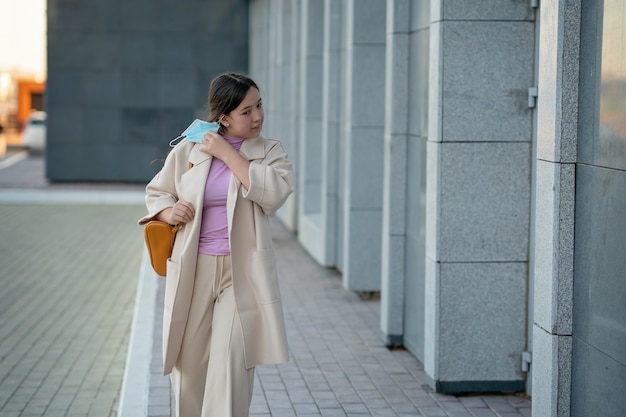 Stylish girl walks down the street and takes off a medical mask from her face