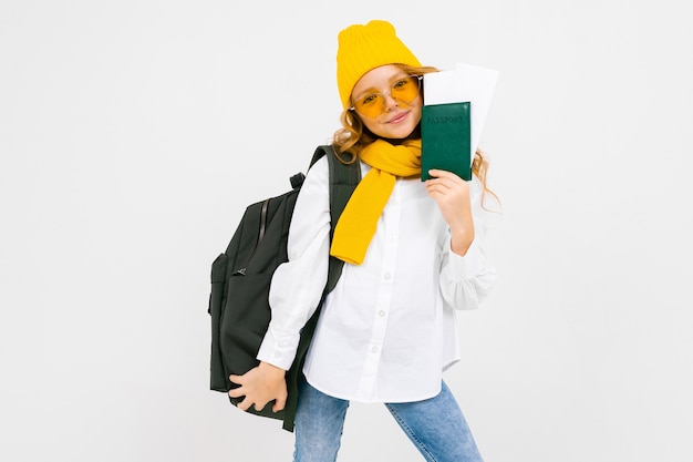 Stylish girl with a backpack on her shoulders holds a passport with vacation tickets on a white background with copy space.