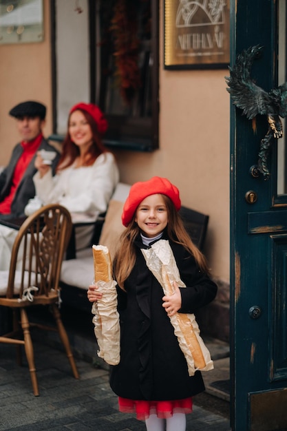 A stylish girl with baguettes stands near the store against the background of her parents