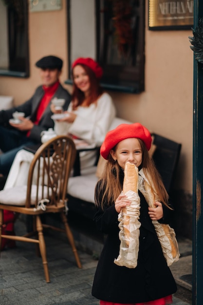 A stylish girl with baguettes stands near the store against the background of her parents