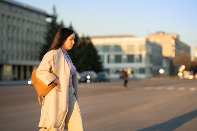 stylish girl with long hair and a backpack behind her shoulders crosses the road to the green light