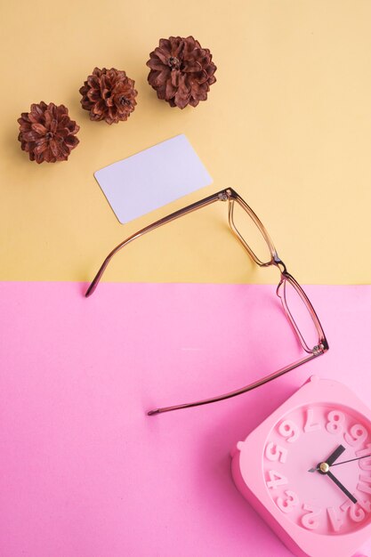 Photo stylish glasses over pastel background. business card, pastel pink and yellow colors. alarm clock, fir tree flowers.