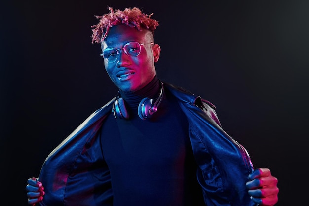 Stylish glasses and wireless headphones Futuristic neon lighting Young african american man in the studio