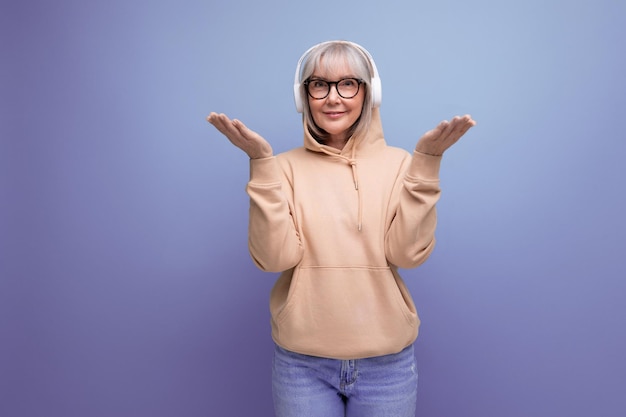 Stylish grandmother with gray hair masters technique and listens to music in headphones on a studio