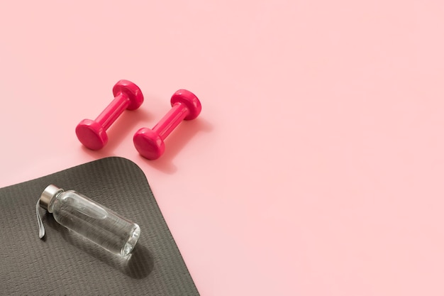 Photo stylish gray and pink fitness training and gym concept perspective view of gray sport mat water bottle and pink dumbbells on pink background set for pilates fitness with copy space