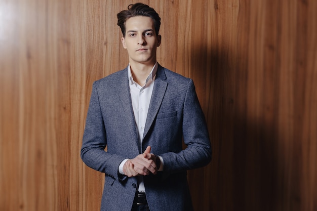 Stylish guy in jacket at office on simple wooden background