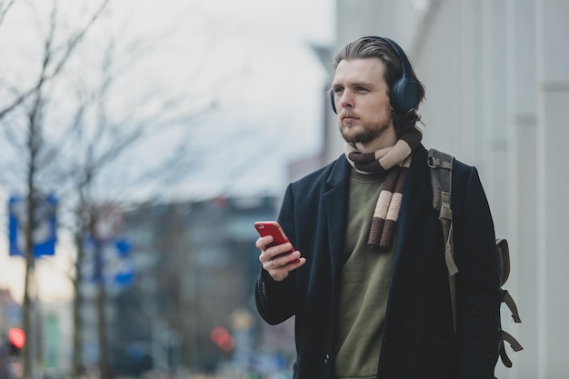 Stylish guy in scarf and coat listen a music on streaming service by using mobile phone at street of Wroclaw Poland