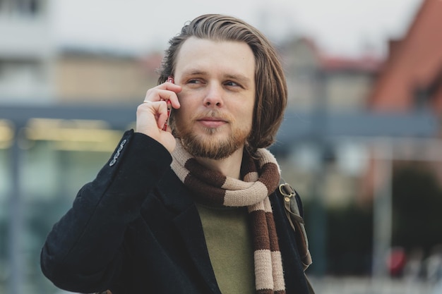 Stylish guy in scarf and coat talking by mobile phone at street of Wroclaw Poland