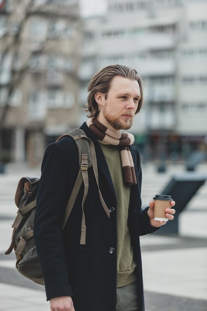 Stylish guy in scarf and coat with takeaway cup of coffee at street of Wroclaw Poland