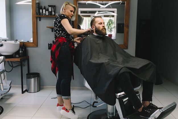 Stylish hairdresser cutting hair of client at barber shop. 