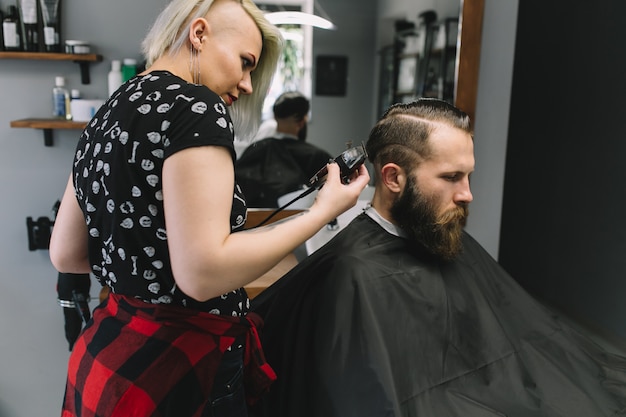 Stylish hairdresser cutting hair of client at barber shop. 