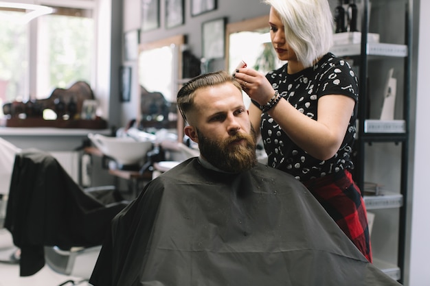 Stylish hairdresser cutting hair of client at barber shop. 