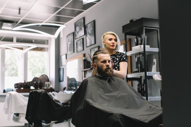 Stylish hairdresser cutting hair of client at barber shop. 