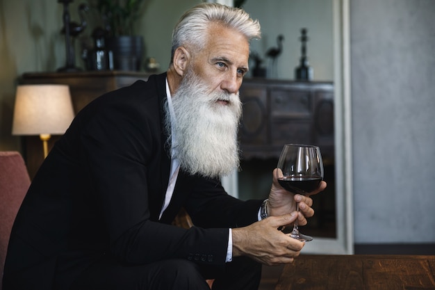 Stylish and handsome bearded senior man drinking red wine