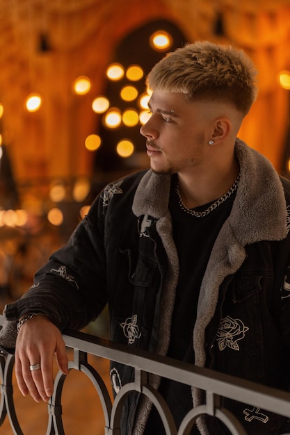 Stylish handsome man model with a hairstyle in fashionable black clothes with a Tshirt and a fashion jacket walks in the mall with lights