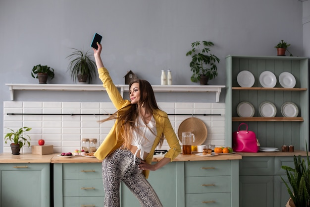 Stylish happy brunette girl in snake printed trousers dancing in the kitchen