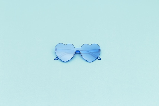 Stylish heart shaped glasses on paper background with copy space Beautiful trendy blue sunglasses