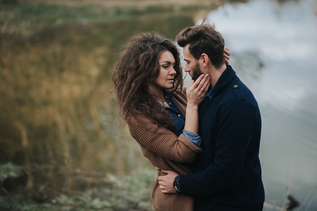 Stylish hipster caucasian couple hugging at lake in autumn. man and woman in love in modern outfit.