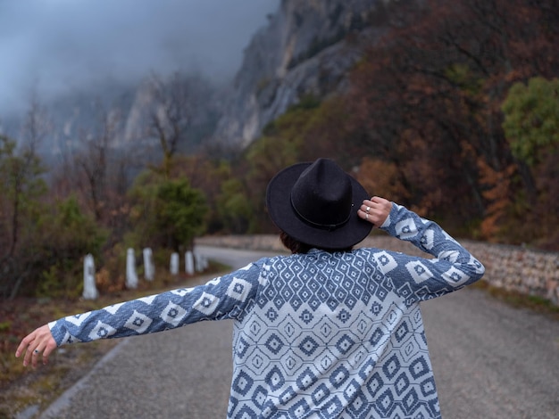 Stylish hipster woman in a hat walking down a mountain road