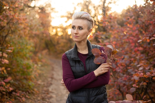 Stylish hipster woman smiling and playing with autumn leaves in park Autumn woman fall