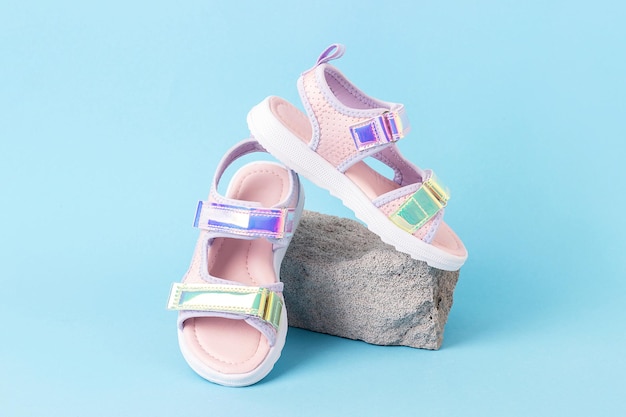 Stylish holographic sandals for kids on grey stone blue background Shiny fashion summer shoes Front view