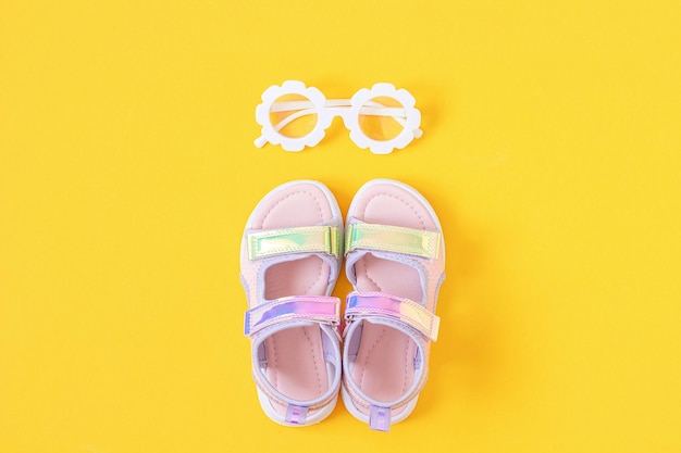 Stylish holographic sandals for kids on yellow background Shiny fashion summer shoes Flat lay Top view