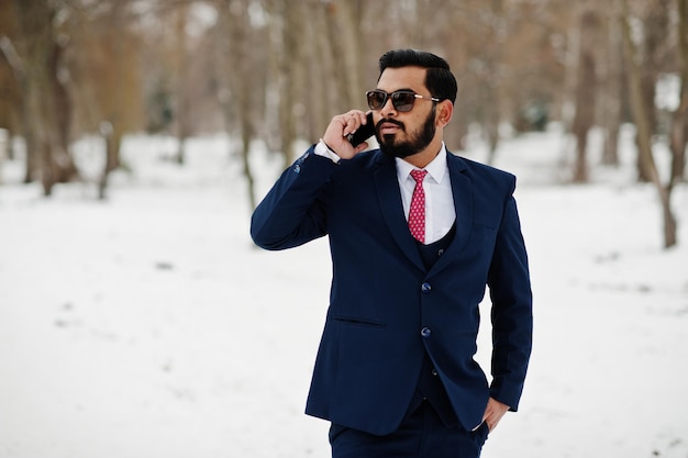 Stylish indian beard business man in suit and sunglasses posed at winter day outdoor speaking on mobile phone