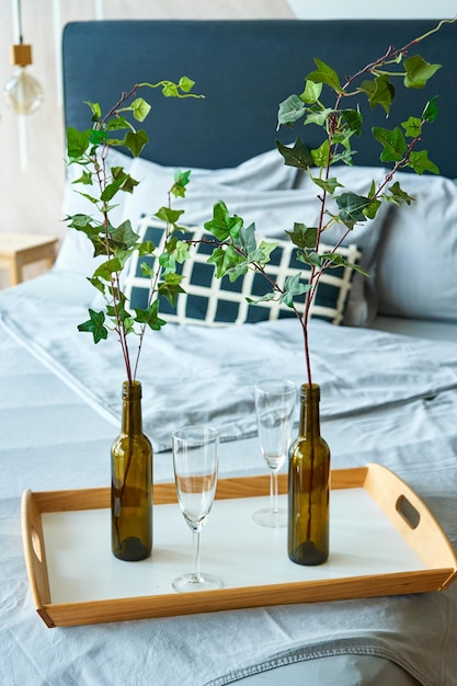 Stylish interior of sleeping room with double bed and branches in vine bottles on the tray