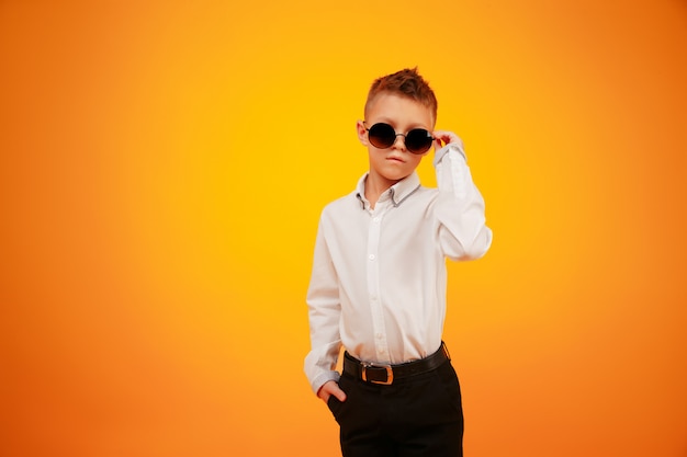 Stylish kid in white shirt and black trousers posing in sunglasses