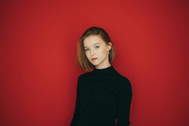 Stylish lady in dark casual clothes isolated on red Beautiful girl in a black sweater