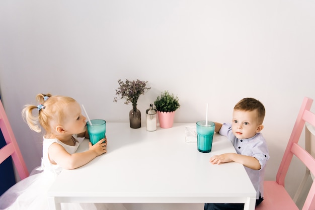 Stylish little boy and girl in a children's cafe drinking a milkshake