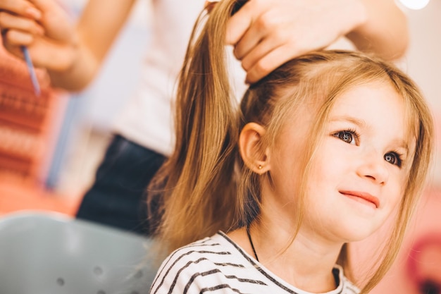 Stylish little girl in a beauty salon for children where she made a beautiful hairstyle Female stylist makes stylish hairstyle to little girl