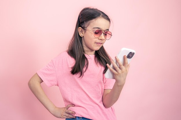 Stylish little girl with a smartphone on a pink background