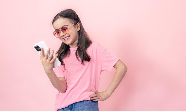 Stylish little girl with a smartphone on a pink background