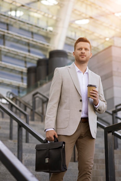 Stylish man going down the stairs while being thoughtful and holding a suitcase