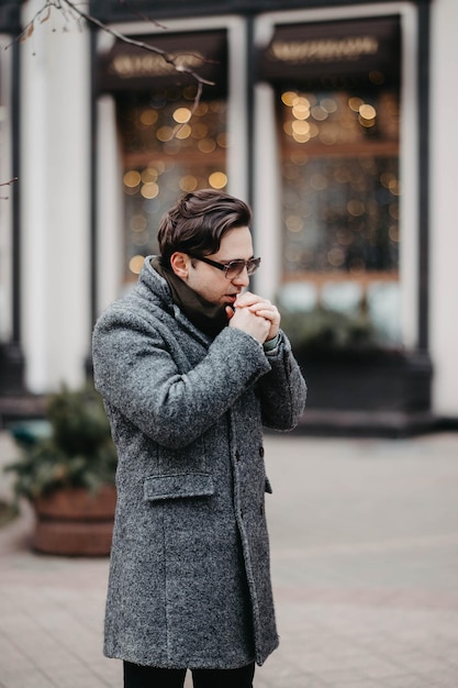 stylish man in a gray coat and sunglasses walking in the city.