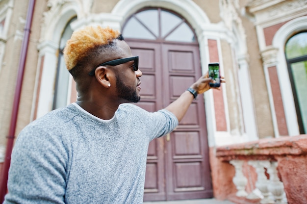 Stylish man on gray sweater and black sunglasses posed on street Fashionable black guy making selfie on phone.