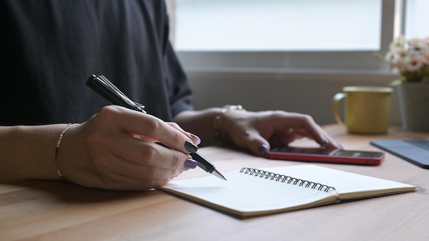 Stylish man hand writing on notebook and using mobile phone for searching information