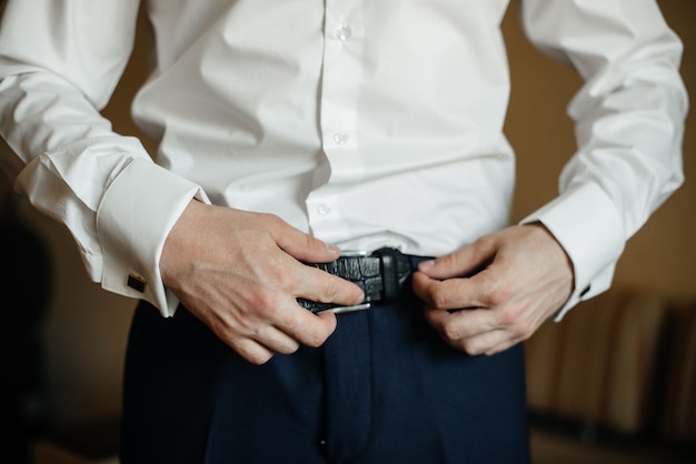 A stylish man puts on a leather belt close-up.