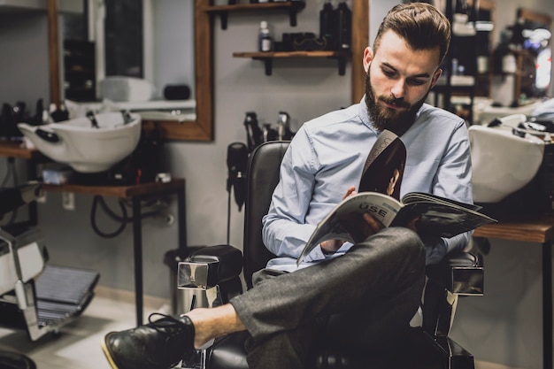 Stylish man with magazine in barbershop