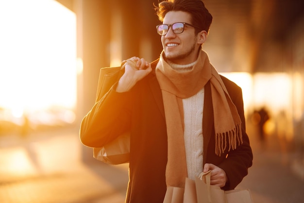 Stylish man with paper packages after shopping at sunset Handsome man doing shopping