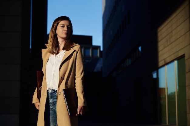 Stylish millennial business woman at city street with laptop business woman wearing coat going to wo