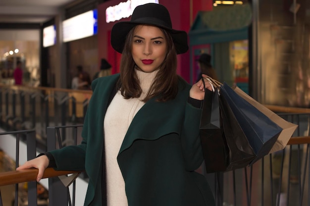 Stylish model in  hat and coat holding shopping bags