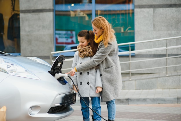 Stylish mother and daughter charge an electric car, and spend time together