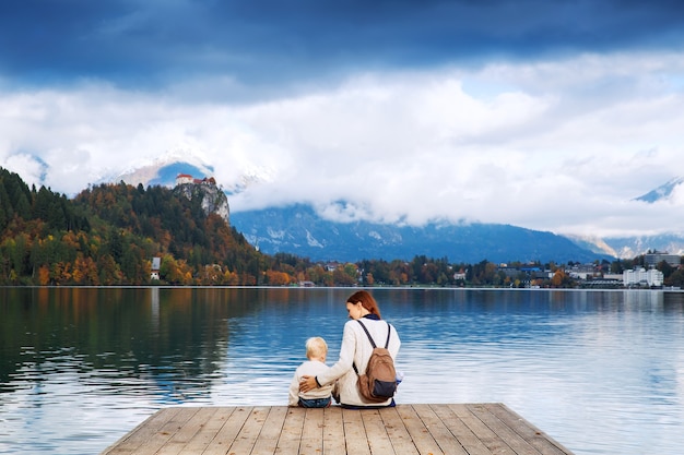 Photo stylish mother and son sitting on a wooden pier on the lake bled slovenia